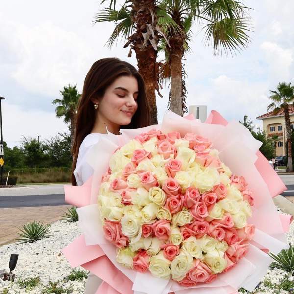 Woman holding a large bouquet of pink and cream roses
