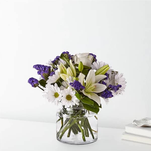 White lilies and daisies in a clear glass vase with purple filler flowers