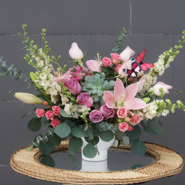Pink and white floral arrangement in a white vase with butterfly accents