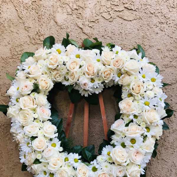 Heart-shaped floral wreath of white roses and daisies on an easel