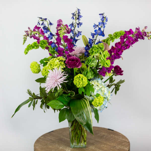Tall mixed bouquet in a clear glass vase with blue, purple, and green flowers
