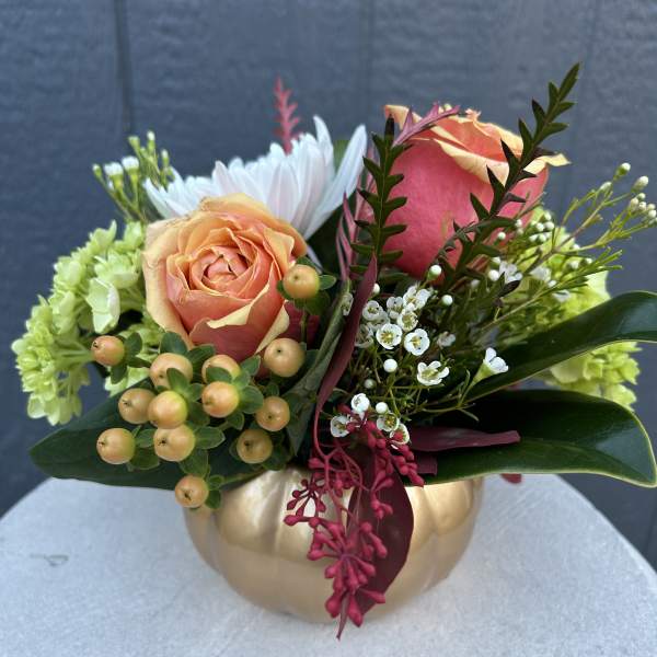 Peach and pink roses arranged in a gold pumpkin vase
