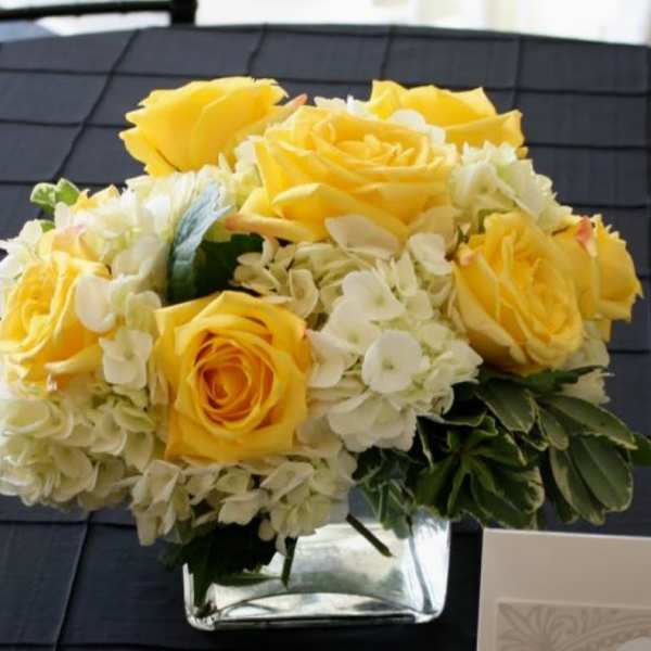 Yellow roses and white hydrangeas in a clear square vase