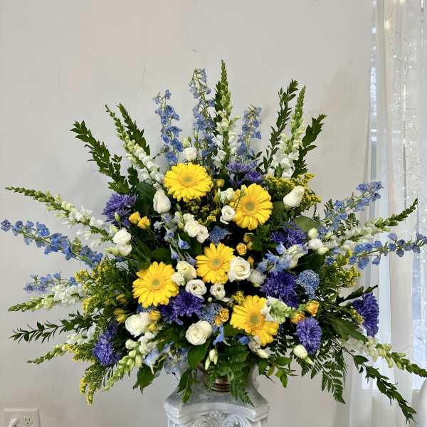 Large floral arrangement with yellow daisies, white roses, and blue-purple flowers in a vase