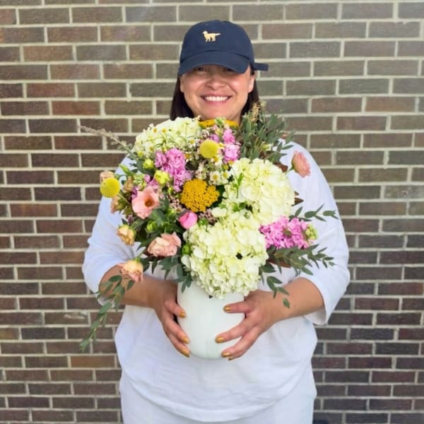 Person holding a colorful flower arrangement in a white vase