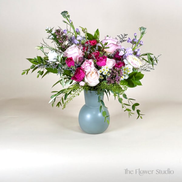 Pink and lavender roses, carnations, and daisies arranged in a matte blue vase.