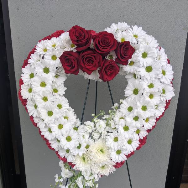 Heart-shaped floral wreath with red roses and white daisies on a stand