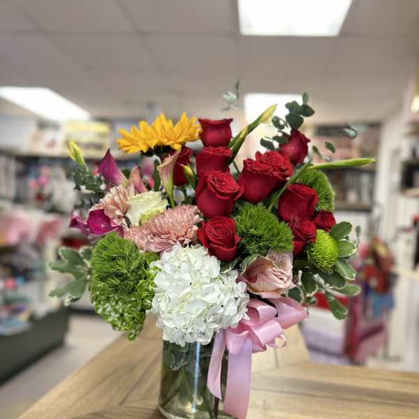 Mixed bouquet of red roses, white hydrangea, and yellow blooms in a glass vase