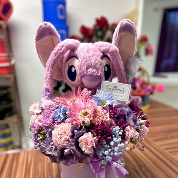 Pink plush bunny holding a mixed bouquet in a round box