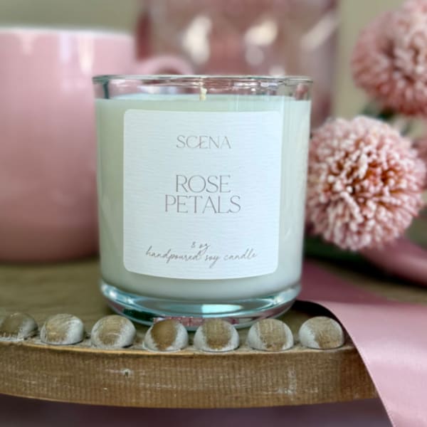 Rose-scented white candle in a clear glass jar with pink mug, flowers, and ribbon on a wooden tray