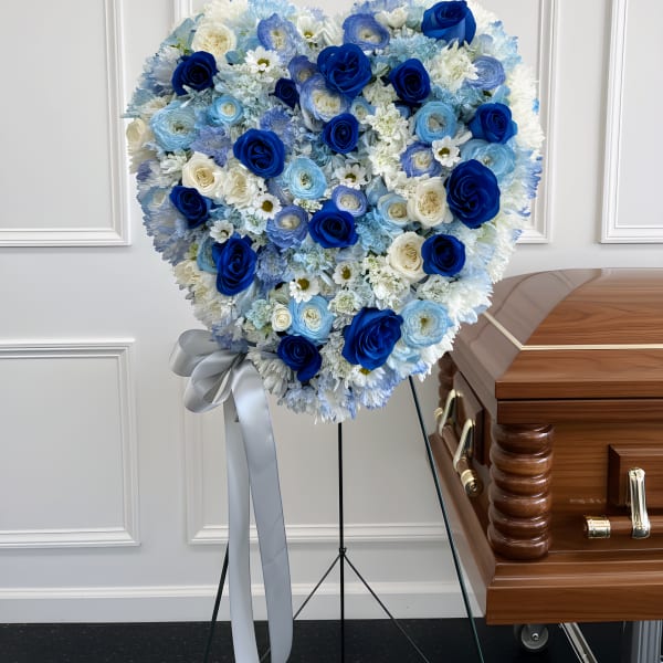 Heart-shaped blue and white floral funeral spray beside a casket