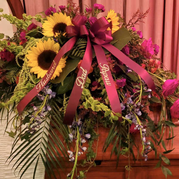 Large floral spray with sunflowers, pink roses, and ribbons