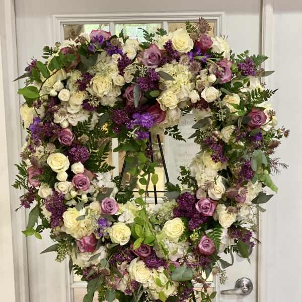Heart-shaped floral wreath on a stand with cream, pink, and purple roses.