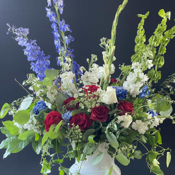 Large bouquet of red and white roses with blue delphinium in a white vase