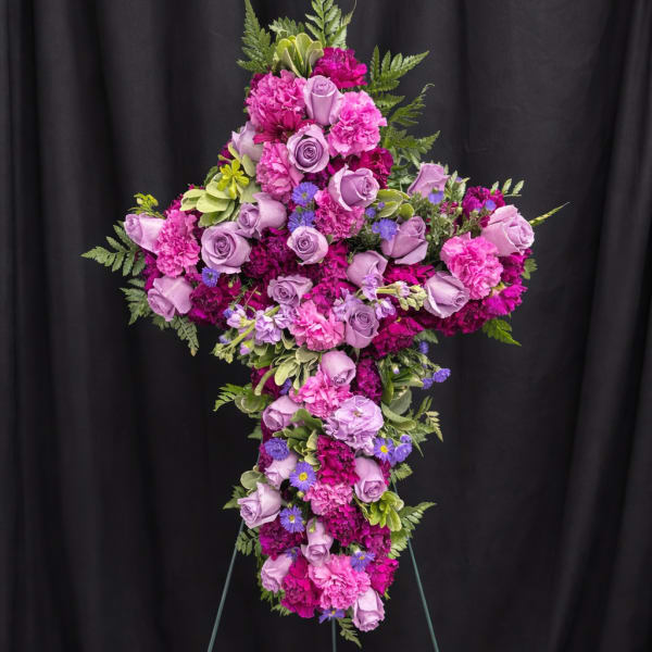 Standing cross-shaped spray of purple roses and bright pink carnations on an easel.