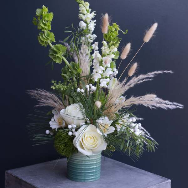 White roses and snapdragons in a teal vase with airy grasses