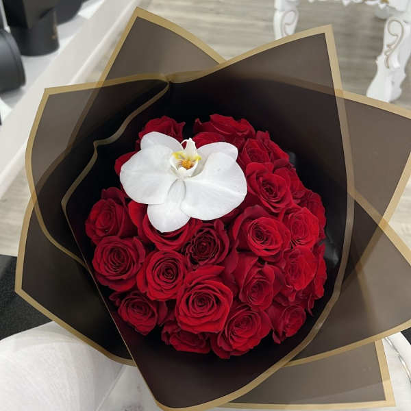 Bouquet of red roses with a white orchid in dark wrap