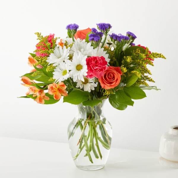Mixed bouquet of daisies, roses, carnations, and purple filler in a glass vase