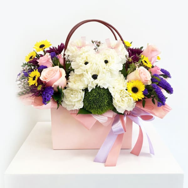 Pink and white floral arrangement in a gift box with a teddy bear face