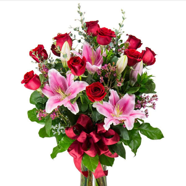 Bouquet of red roses and pink lilies in a glass vase with a red ribbon