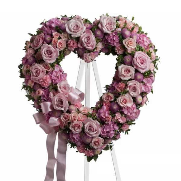 Heart-shaped floral wreath of pink and purple flowers on an easel with ribbon