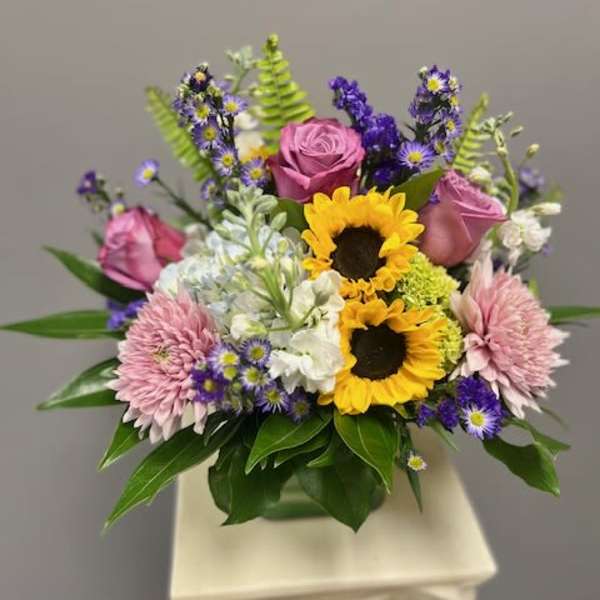 Mixed bouquet with sunflowers, pink roses, and purple flowers in a vase