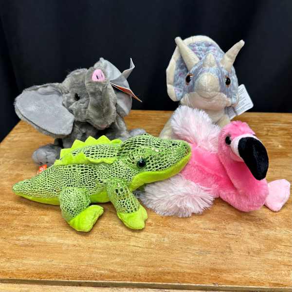 Four plush animal toys on a wooden surface.