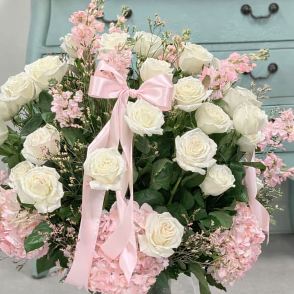 White roses and pink hydrangeas in a glass vase with a pink ribbon