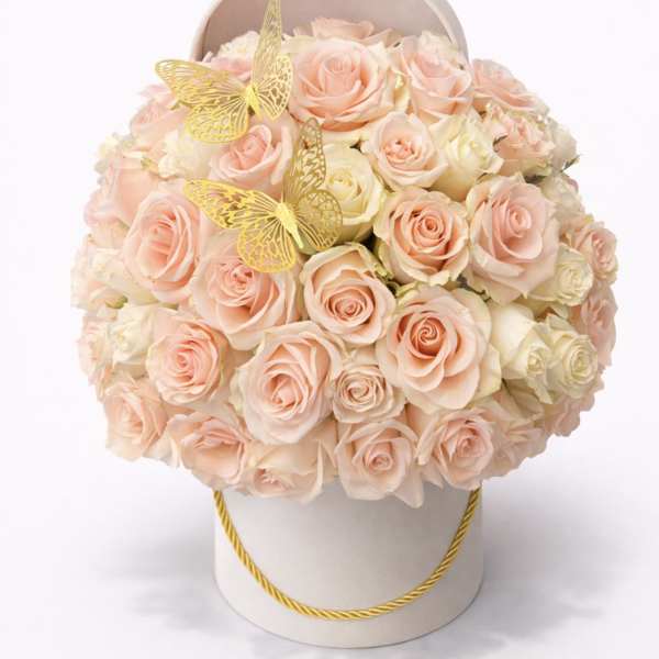Round hatbox arrangement of peach and cream roses accented with two gold butterfly decorations.