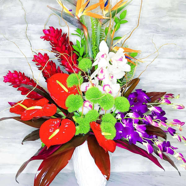 Tropical flower arrangement in a white vase with orchids and red anthuriums