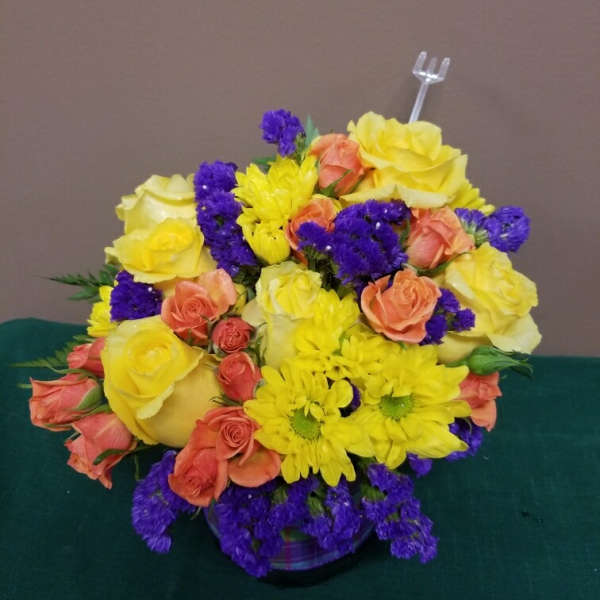 Bouquet of yellow and peach roses with purple filler flowers in a low vase