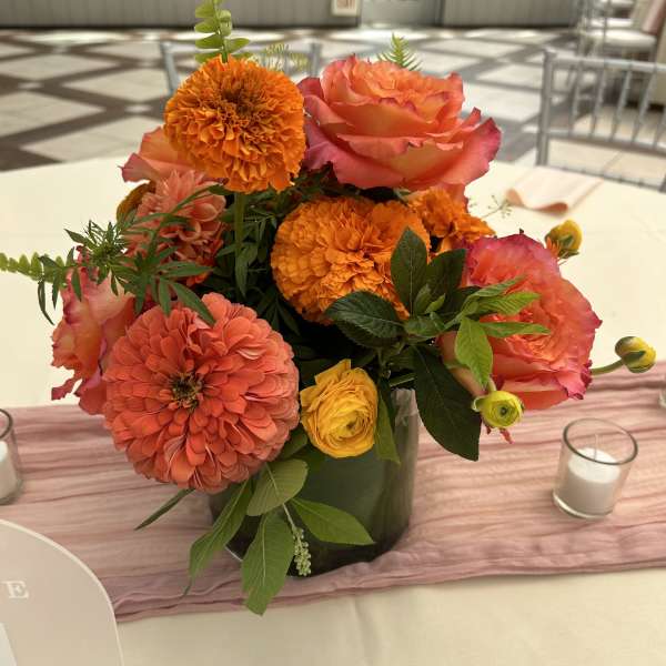 Orange and pink floral centerpiece in a dark vase
