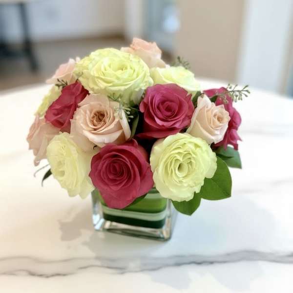 Pink and pale yellow roses arranged in a square glass vase