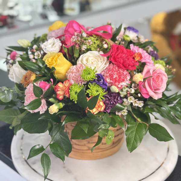 Mixed bouquet in a wicker basket with pink, yellow, white, and purple flowers