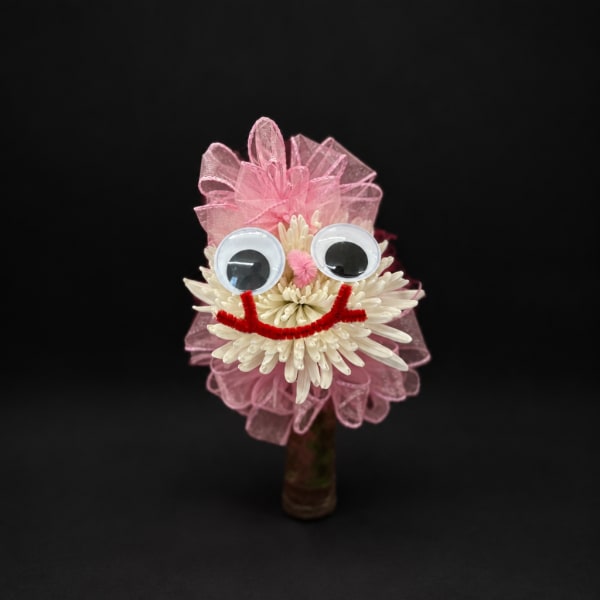 Pink and white flower arrangement with googly eyes and a smile