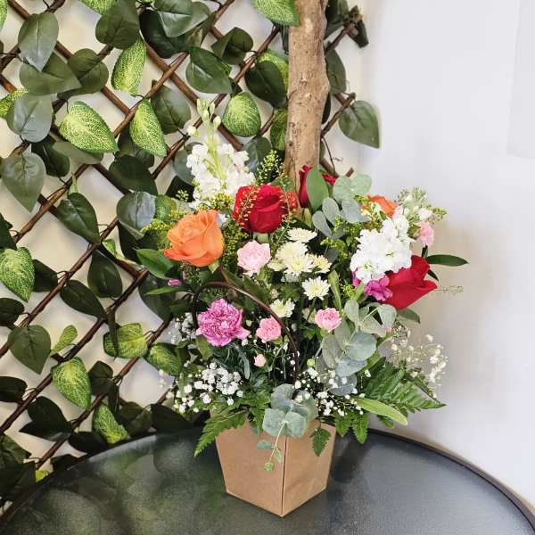 Mixed bouquet of roses, carnations, and white filler flowers in a paper box