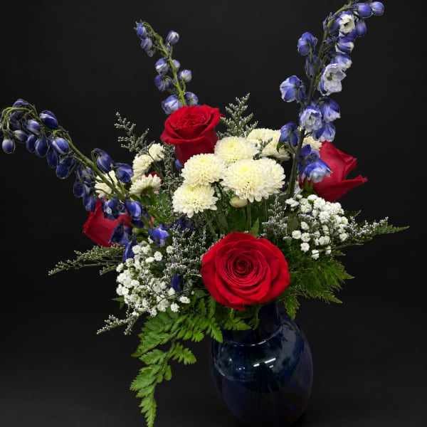 Red roses and white mums in a blue glass vase with blue flowers