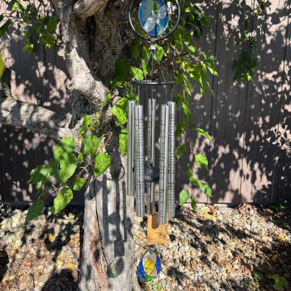Stained-glass and metal wind chime hanging from a tree branch
