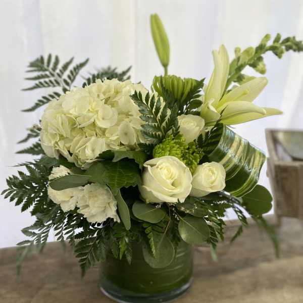 Low white and green flower arrangement with hydrangea, roses, and lilies in a green-lined glass vase