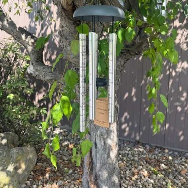 A silver wind chime hanging from a tree branch outdoors.