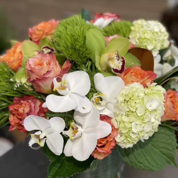 Bouquet of white orchids, peach roses, and pale hydrangeas in a glass vase