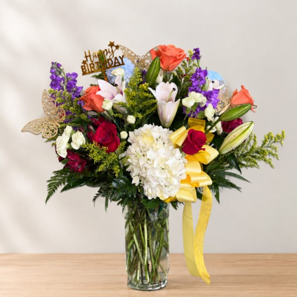 Mixed bouquet of roses, lilies, and hydrangea in a glass vase with a birthday topper