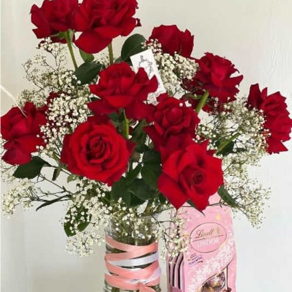 Bouquet of red roses with baby's breath in a glass vase beside a pink candy box