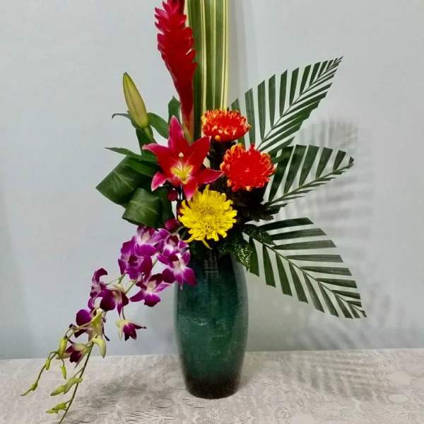 Tropical flower arrangement in a tall green vase with red, yellow, and purple blooms