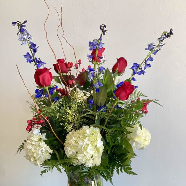 Tall bouquet of red roses, white hydrangeas, and blue flowers in a glass vase