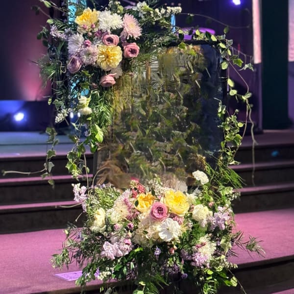 Large floral arrangement with pastel blooms and trailing greenery on a stand