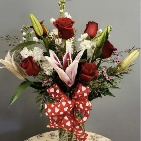 Red roses and lilies in a glass vase with a heart-patterned ribbon