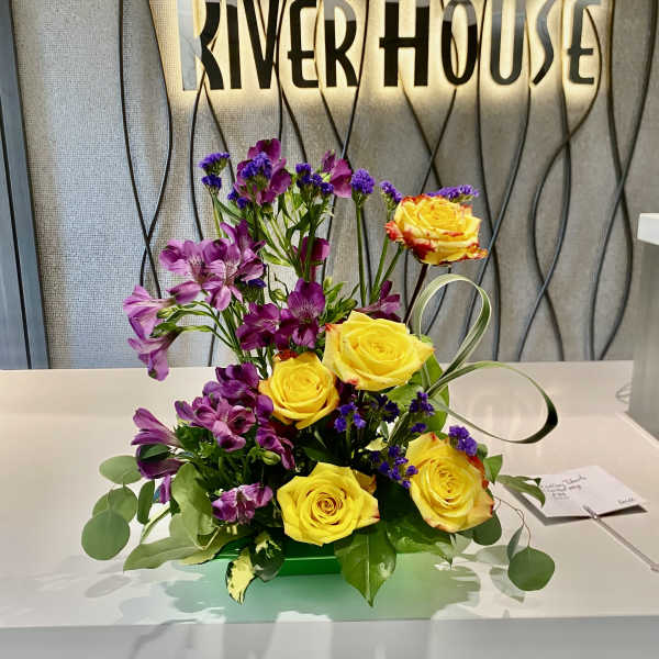 Yellow roses and purple flowers arranged in a low centerpiece