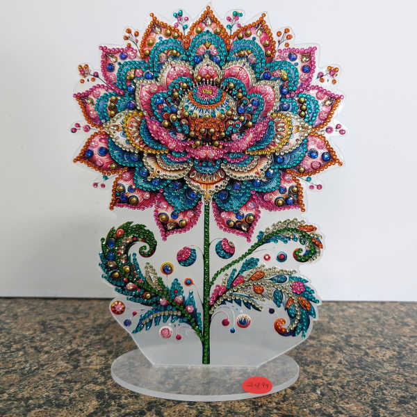 Colorful jeweled floral ornament shaped like a stylized flower on a clear acrylic stand.