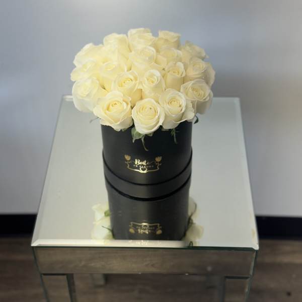 Cream roses arranged in a black round box on a mirrored table